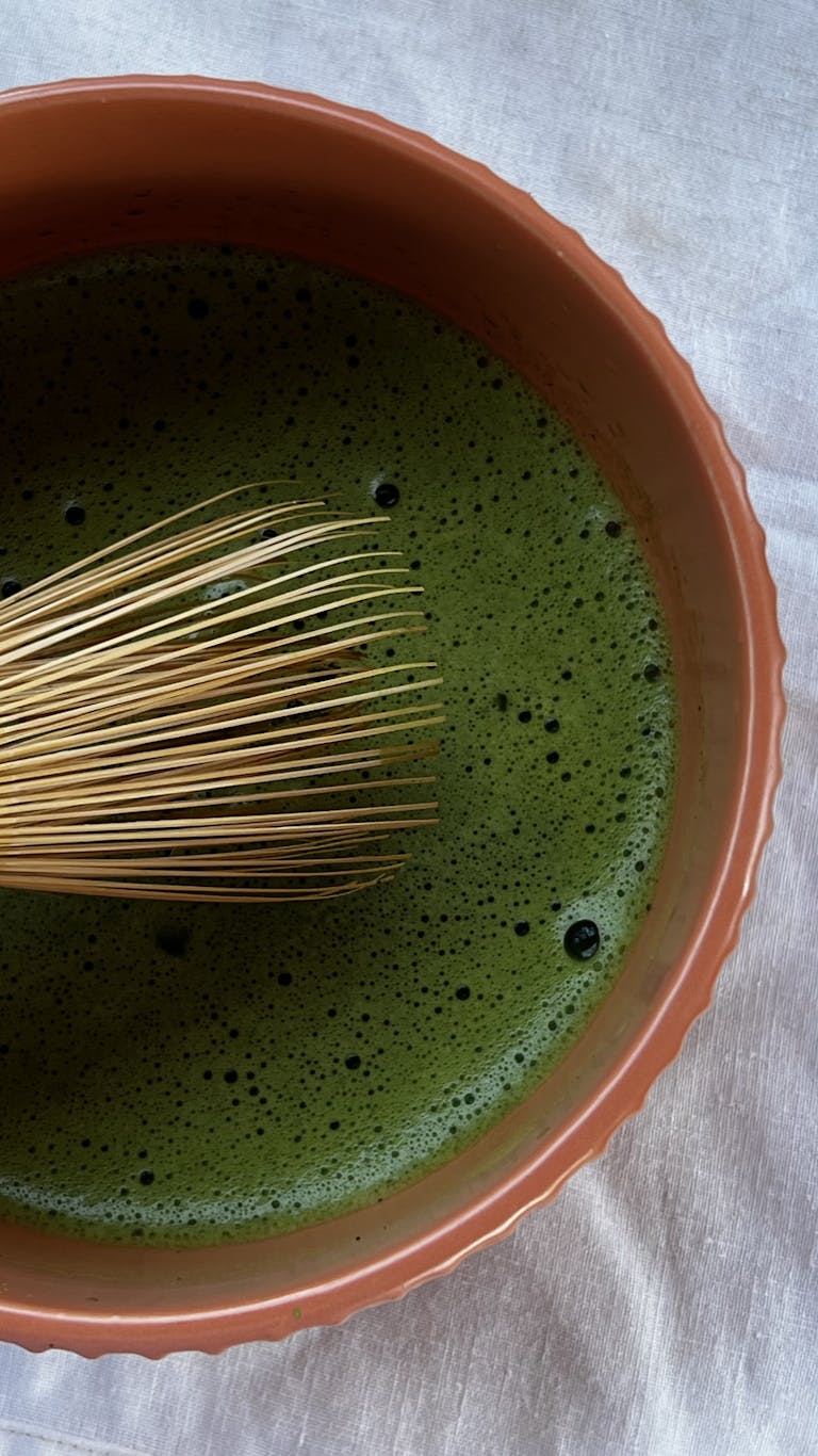 Elegant shot of frothy matcha tea in a ceramic bowl with a traditional bamboo whisk.
