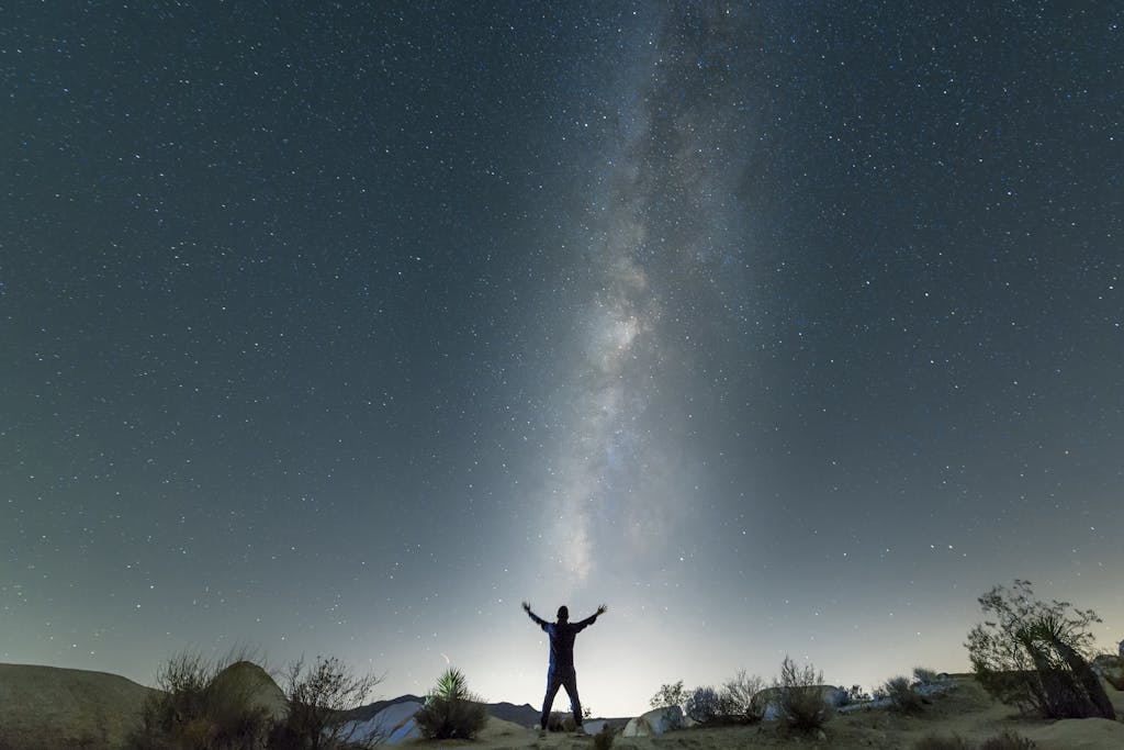 A person stands under the Milky Way in a desert night sky, showcasing the vastness of the universe.