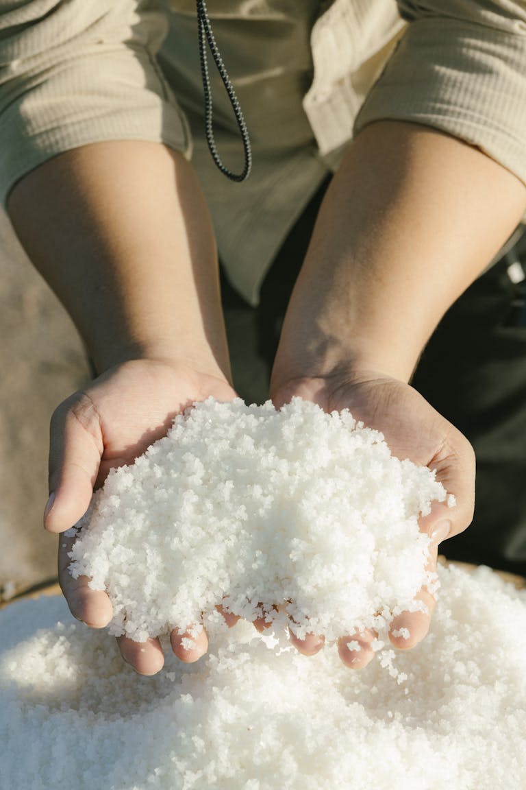 Close-up of hands holding white sea salt crystals outdoors in sunlight.