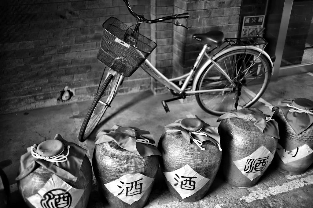Monochrome image showcasing a vintage bicycle parked beside traditional sake jars.