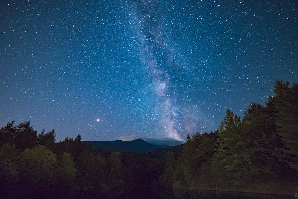 A breathtaking view of the Milky Way galaxy shining brightly over a serene forest landscape at night.